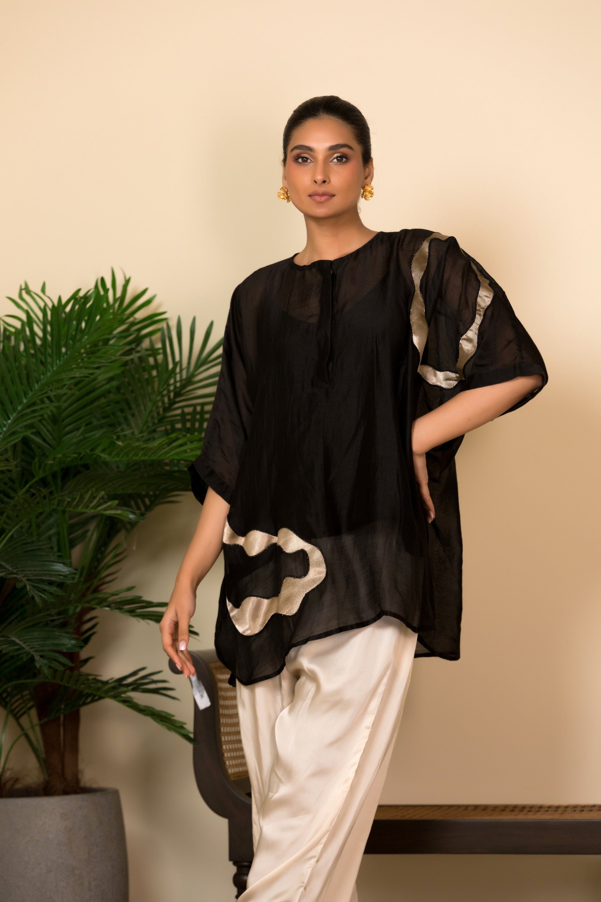 Black silk Indo-Western shirt with handcrafted patch detailing for women, styled with ivory trousers for contemporary Indian wear.